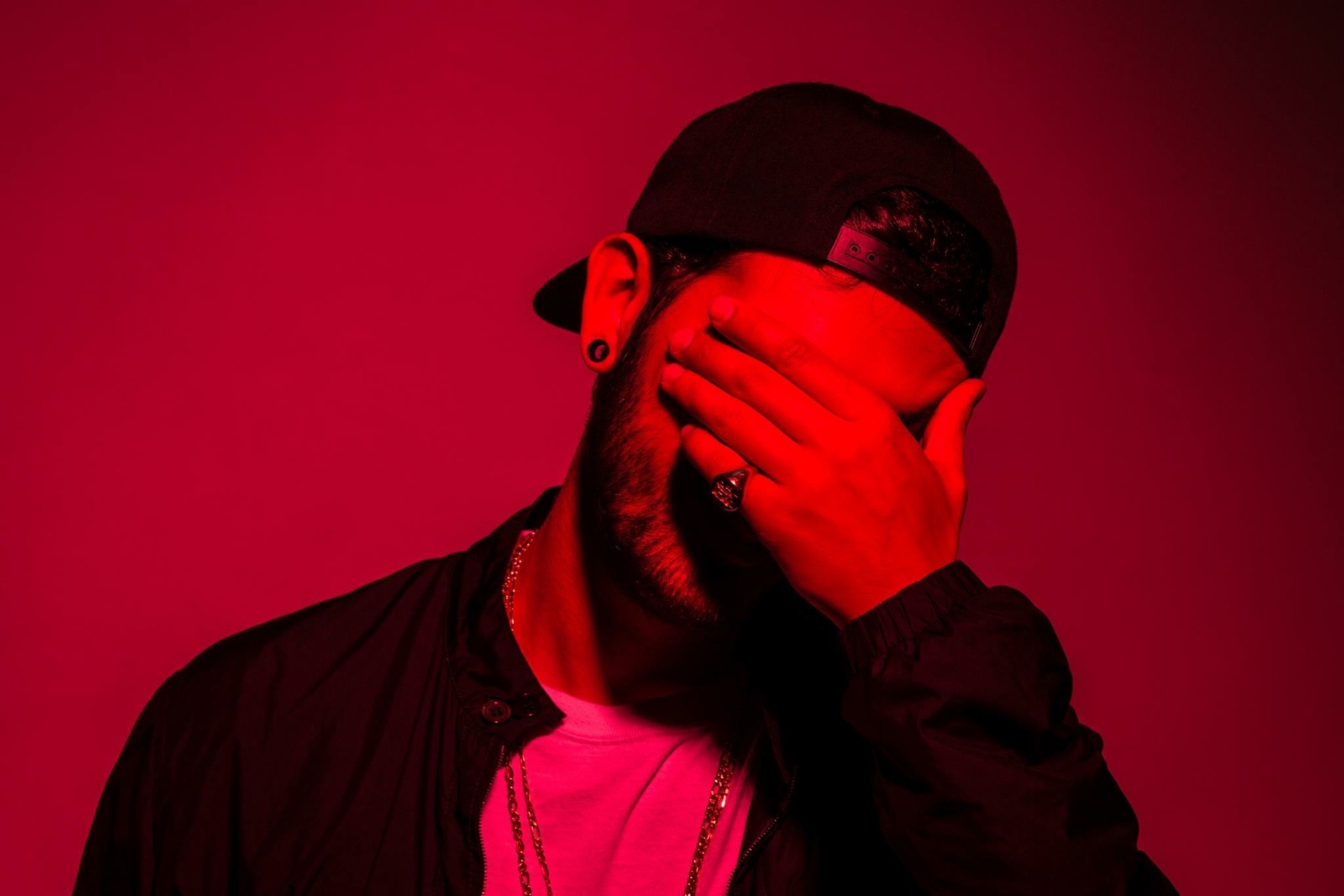 Borgore on a red background with his hand over his face
