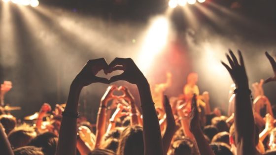 A crowd at a music show, a person holds up their hands in the shape of heart
