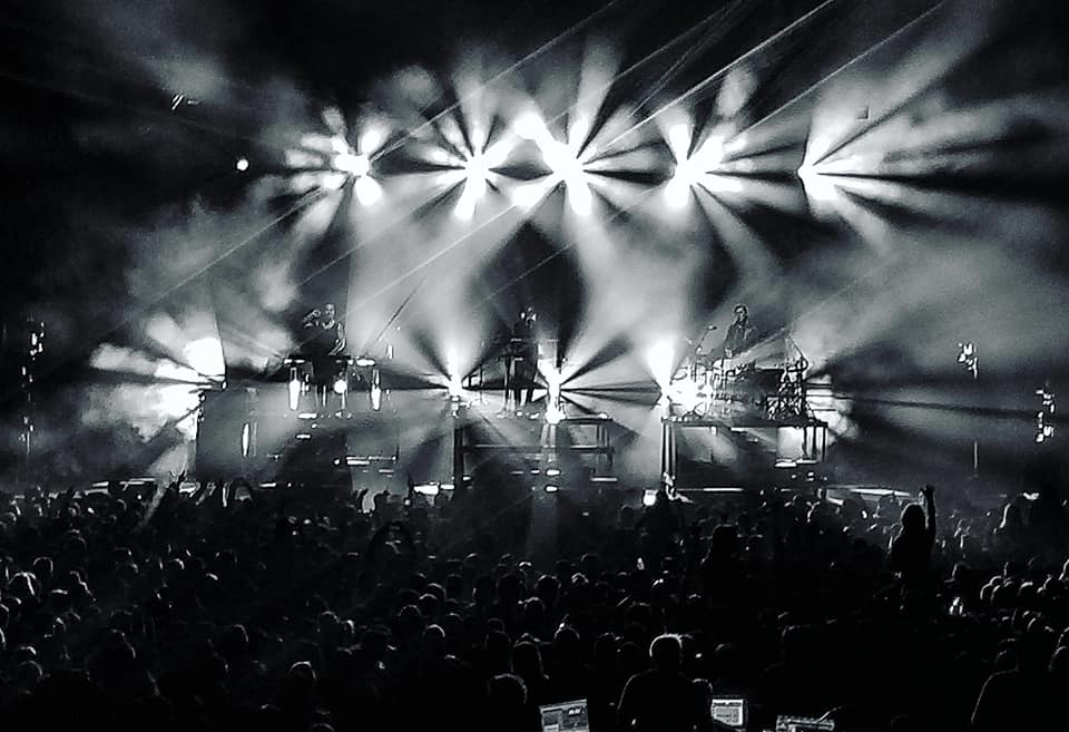 Black and white photograph depicts bright stage lights and a large crowd.