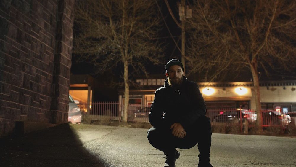 Elazion crouching next to a building at nighttime with trees in the background