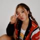 CHYL sitting against a white backdrop in a red jacket giving a peace sign