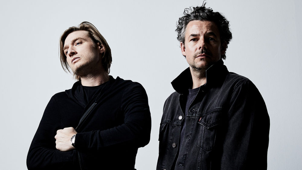 The Midnight's two band members standing in front of a white background wearing black clothes