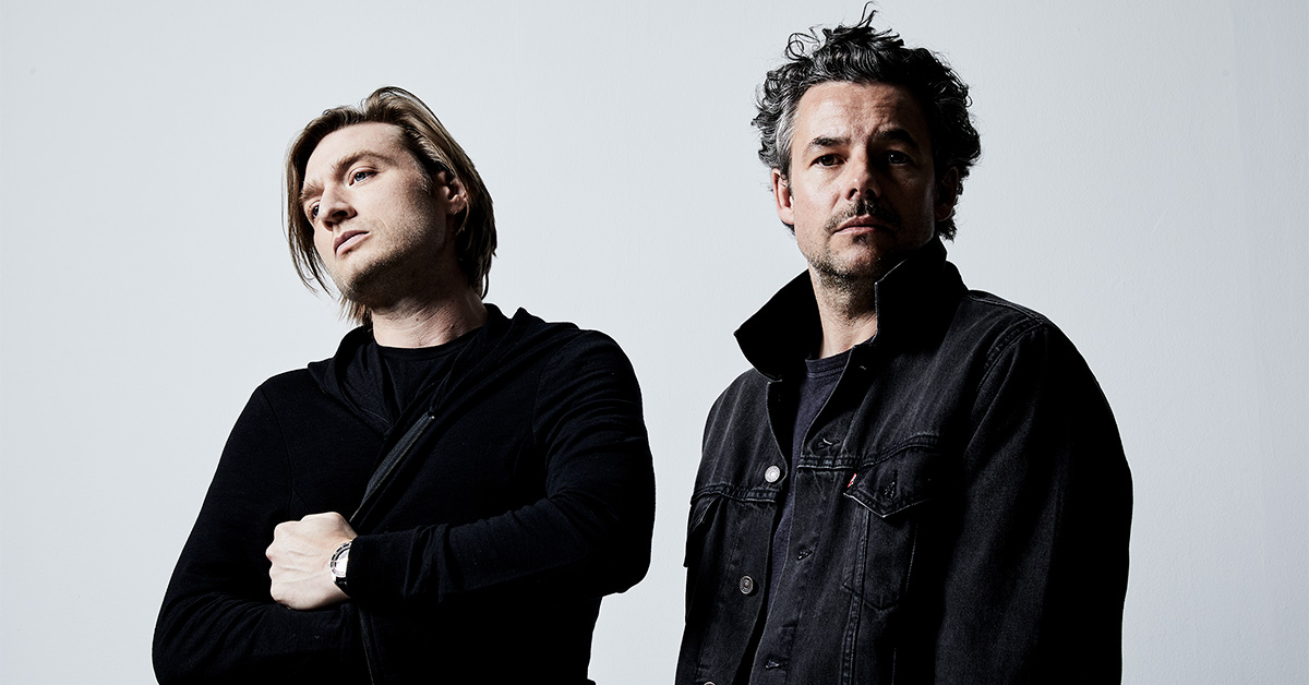 The Midnight's two band members standing in front of a white background wearing black clothes