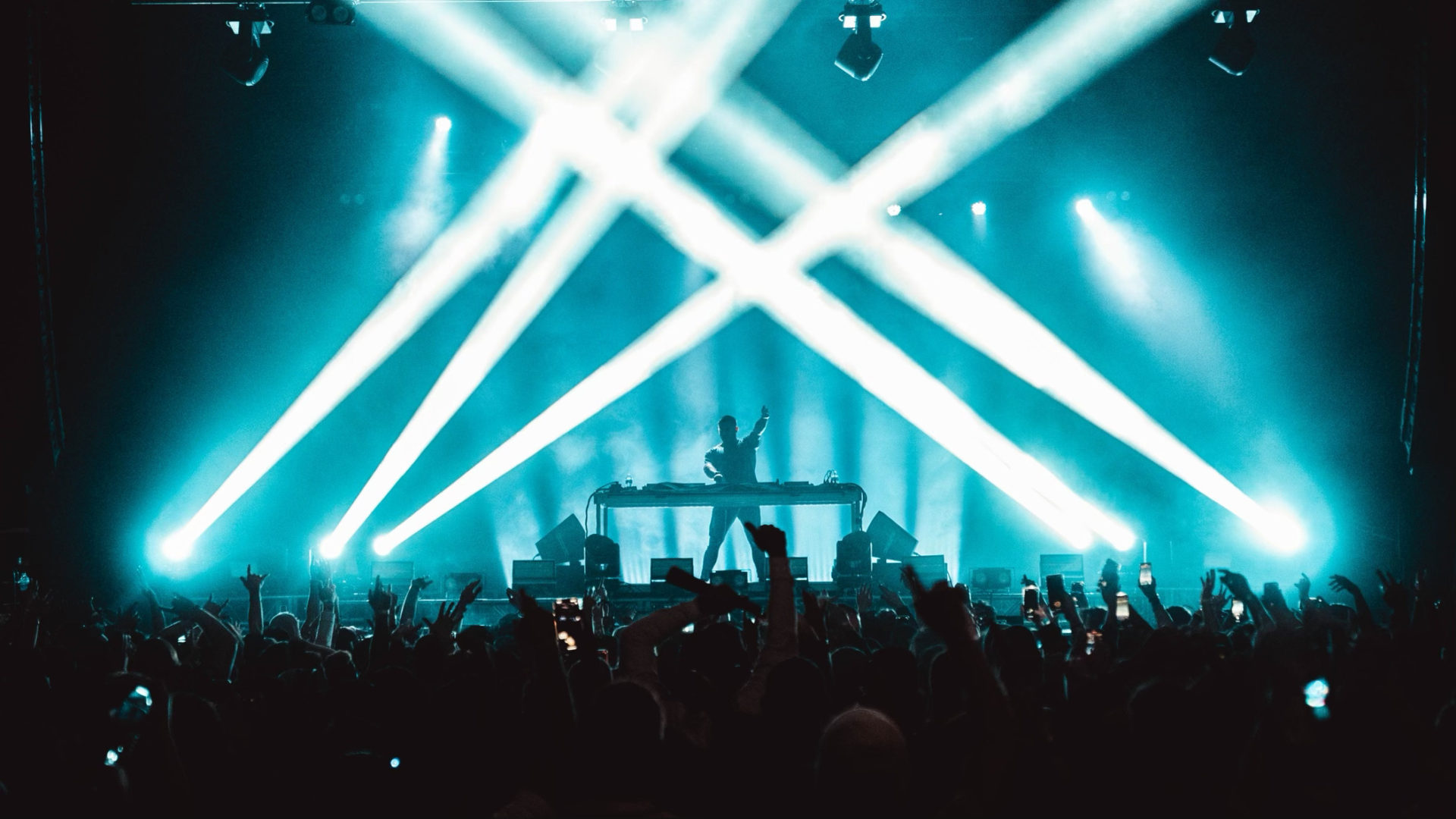 Kai Wachi on stage with his arm up with white spotlights making a triangle above his head in neon blue smoke