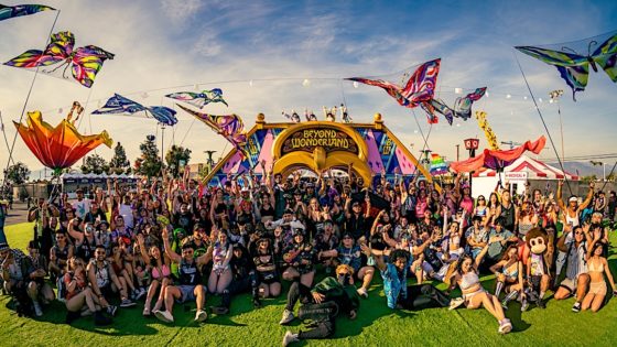 Big group of hundreds festival goers posing for picture in front of Beyond Wonderland arch entrance during daytime.