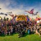 Big group of hundreds festival goers posing for picture in front of Beyond Wonderland arch entrance during daytime.