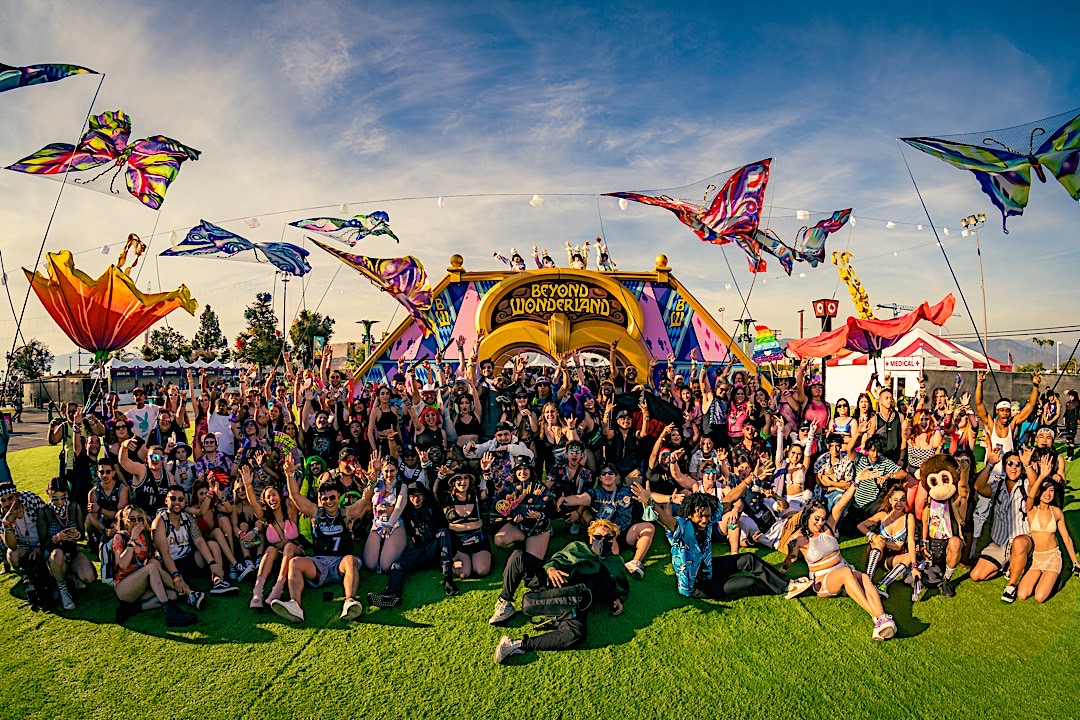 Big group of hundreds festival goers posing for picture in front of Beyond Wonderland arch entrance during daytime.