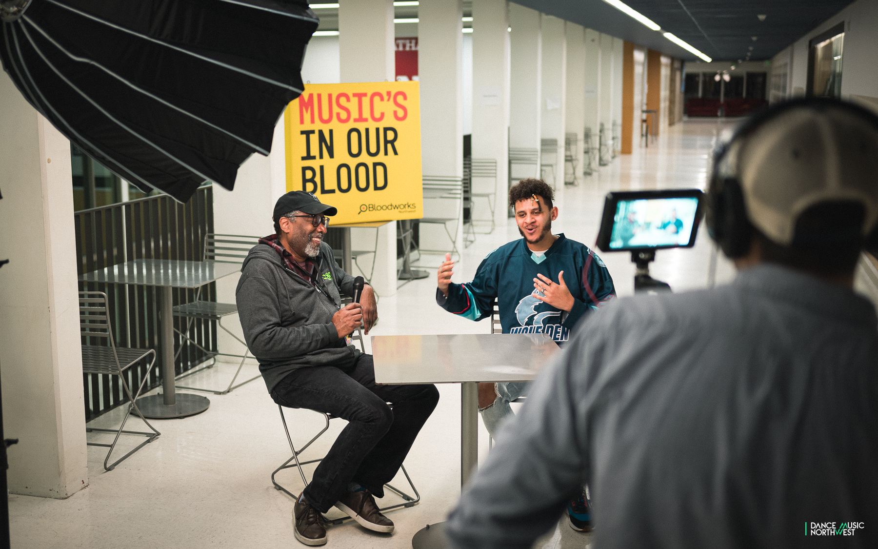 Ron Chatman sits with Marshall Hugh on camera with a white red and black "music's in our blood" poster behind them