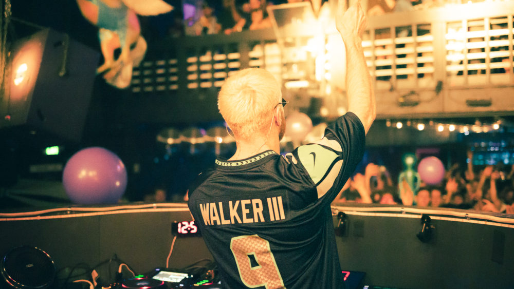 Photo from behind James Hype at DJ booth, wearing #9 Seahawks jersey in front of nightclub crowd.