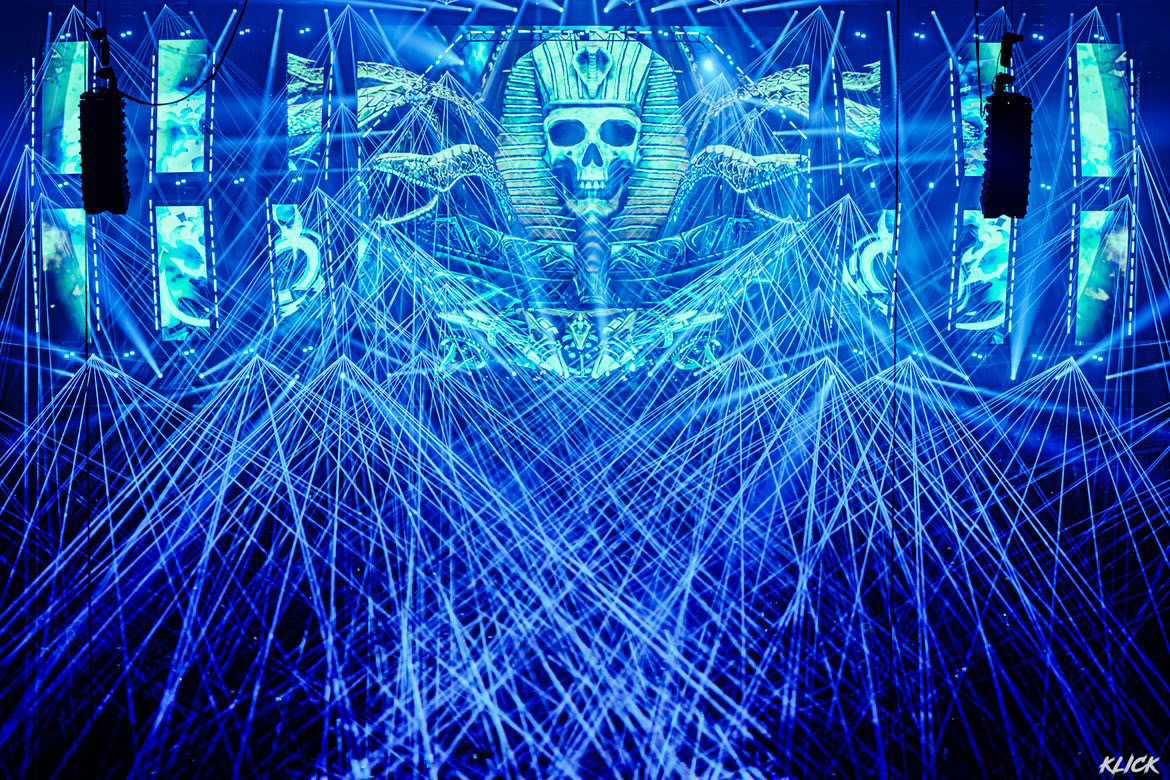 A photo of the stage at Thunderdome 2023. A blue skull of a pharaoh with snakes coming out of its head. Blue lasers shooting out into the crowd and in all directions.