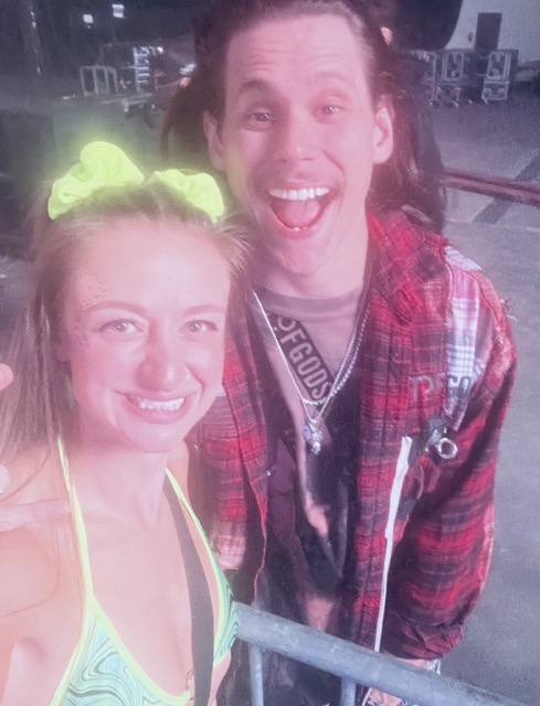 A selfie photo of Sullivan King and Nikki. Sullivan king is pictured in a red flannel and Nikki is wearing neon green. This photo was taken at Thunderdome 2023. 