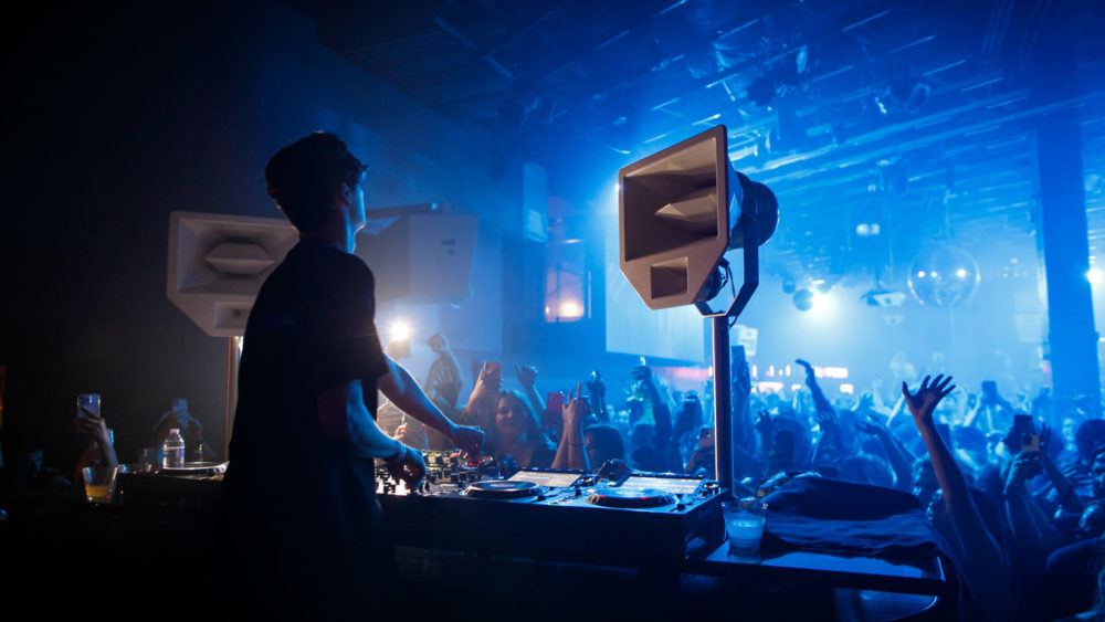 Picture from behind Mau P performing at Q nightclub, with blue lights and crowd in background.