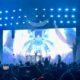 A photo of Seven Lions taken at the Tacoma Dome during the Beyond the Veil tour. Seven lions is seen Djing with his hands in the air. The background shows a blue crystal dome with blue lighting.