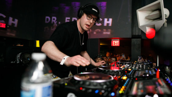 Dr Fresch DJ'ing at Q Nightclub with DJ deck in view at front, Dr Fresch logo projected behind him with purple hue.