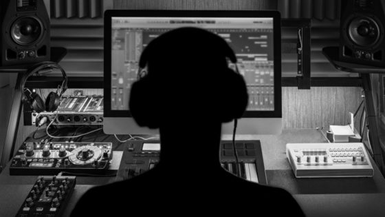 Black and white picture of a man in front of a computer with headphones on creating music