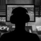 Black and white picture of a man in front of a computer with headphones on creating music