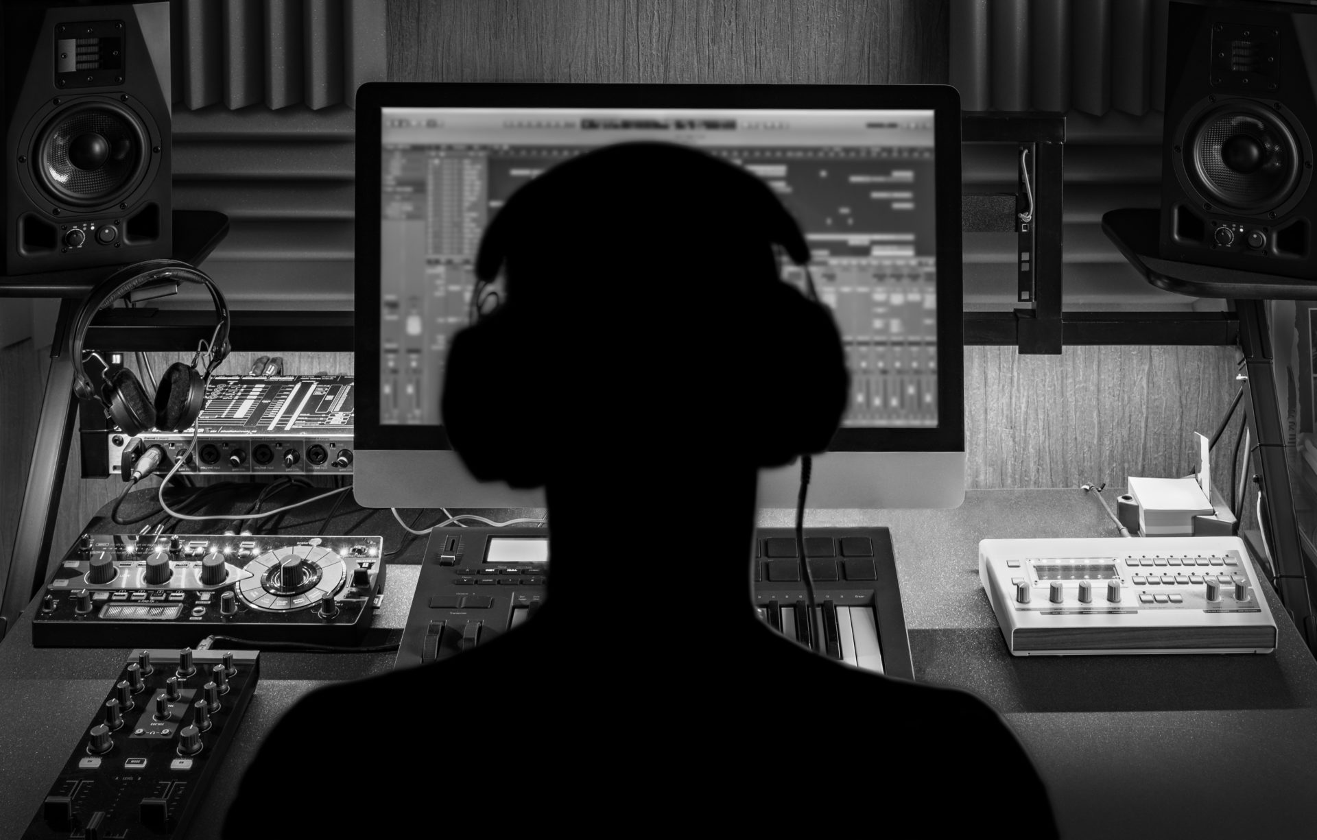 Black and white picture of a man in front of a computer with headphones on creating music