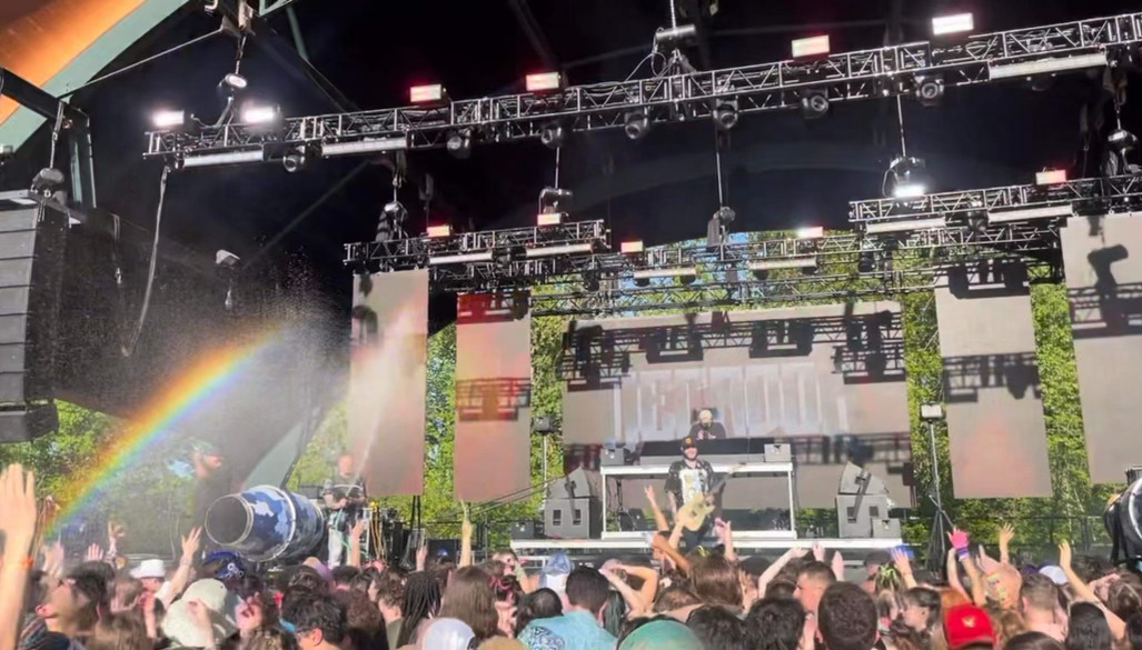Decadon performing with his guitar as a rainbow shows through the mist of water being sprayed