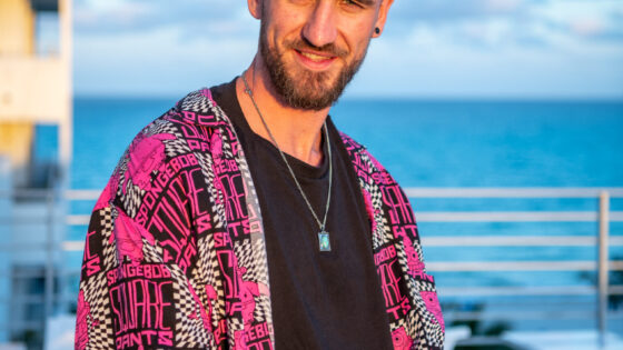 Billy Gillies wearing a red flannel and standing in front of water.