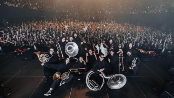 Apashe and brass orchestra posing for picture with crowd in background at Denver show