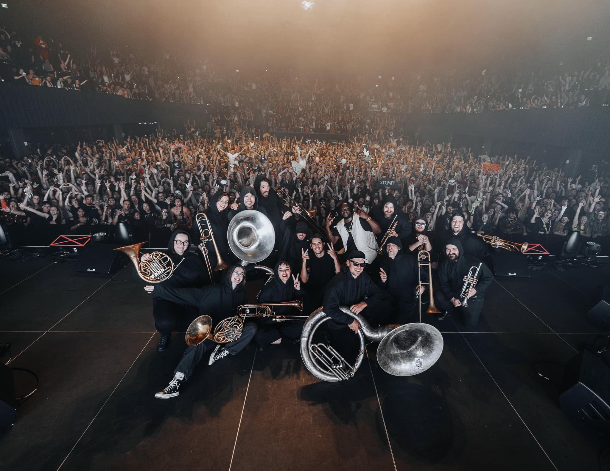 Apashe and brass orchestra posing for picture with crowd in background at Denver show