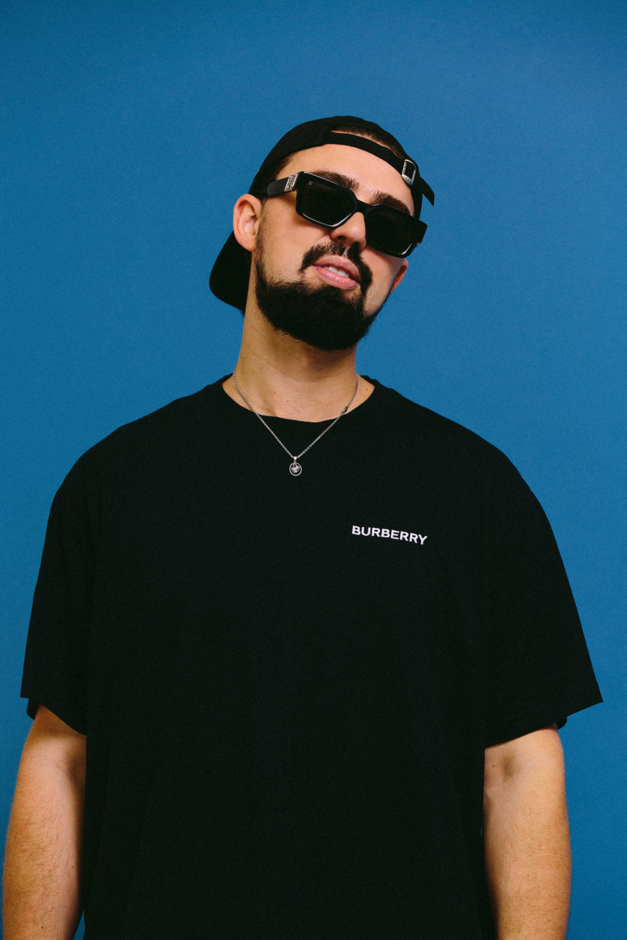 Sonny Fodera wearing a black shirt and standing in front of a blue screen