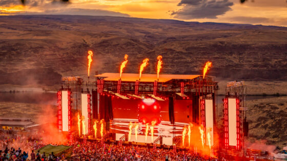 The Bass Canyon main stage is lit up with red lights as the sun sets in the background at the Columbia River Gorge