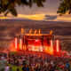 The Bass Canyon main stage is lit up with red lights as the sun sets in the background at the Columbia River Gorge