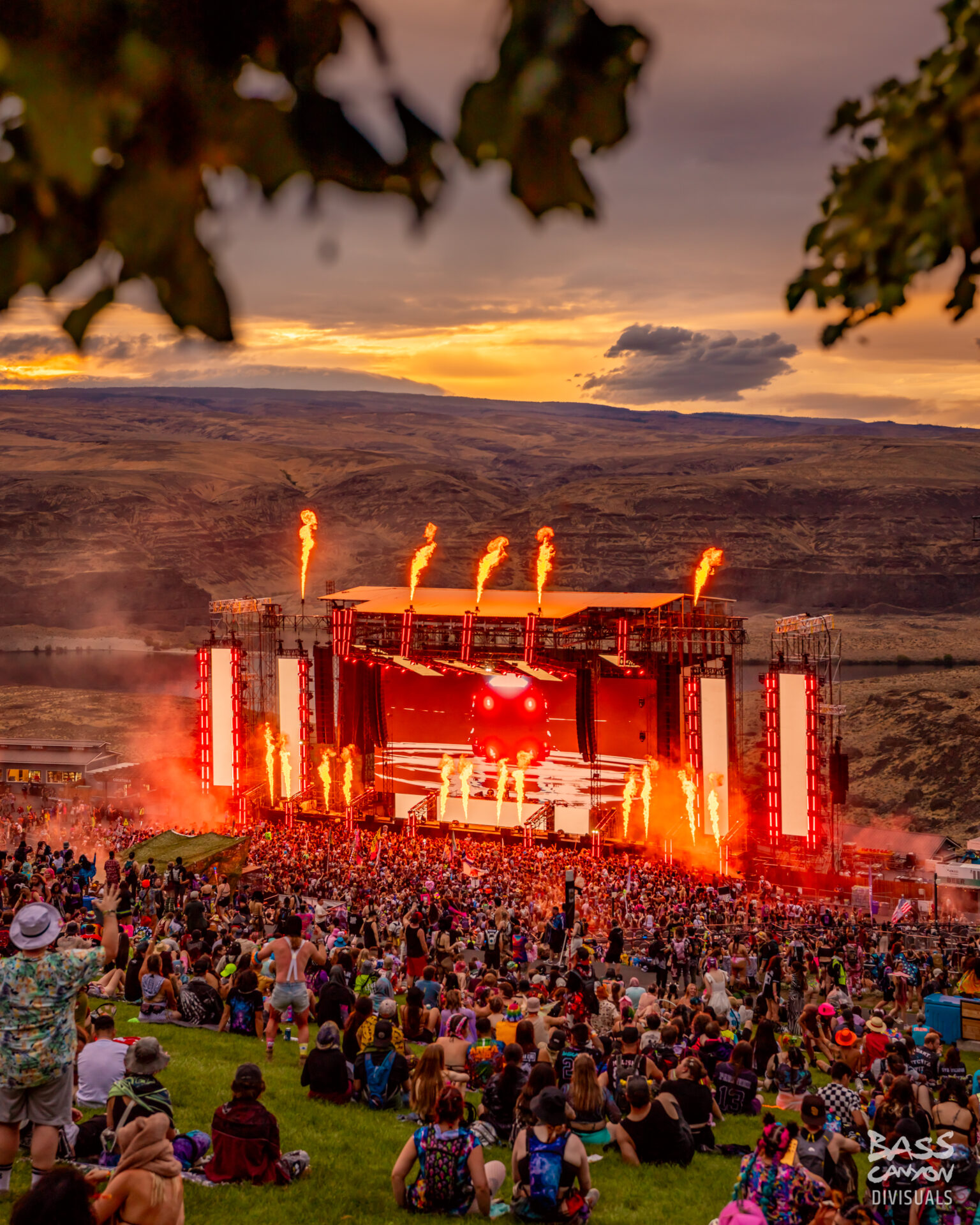 The Bass Canyon main stage is lit up with red lights as the sun sets in the background at the Columbia River Gorge