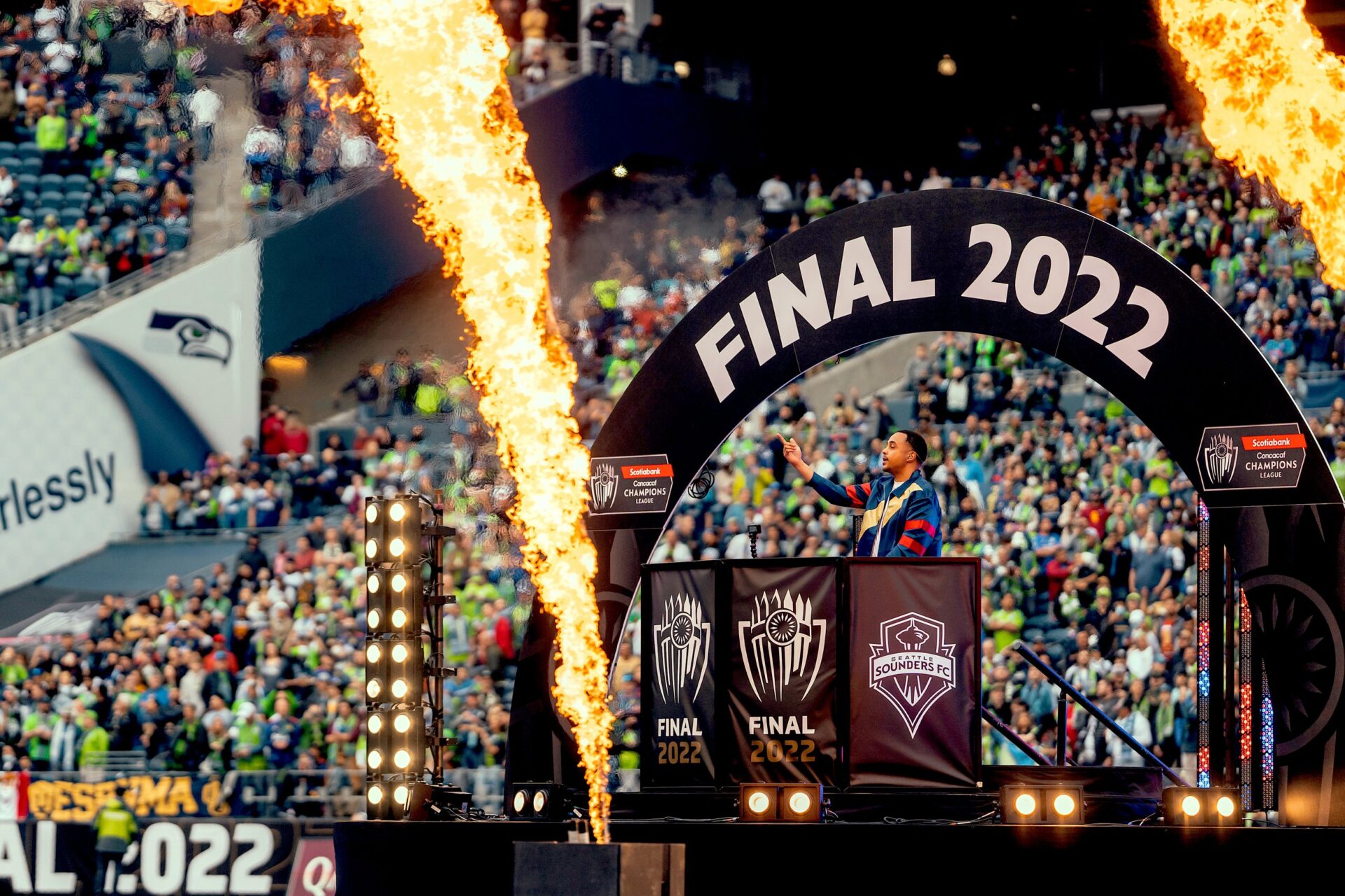 Chris Charma at the DJ booth at the 2022 Seattle Sounders MLS Final 2022, raising his hand while fire cannons erupt in front of him