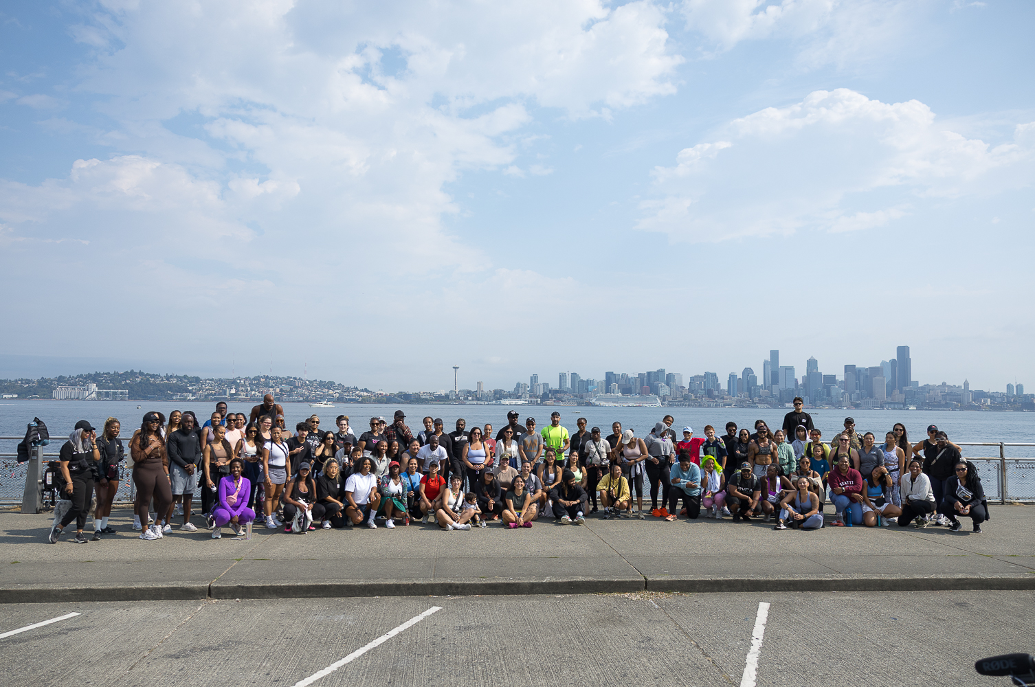 The Walk Club participants standing on the shore at Alki Beach with the Seattle skyline in the background